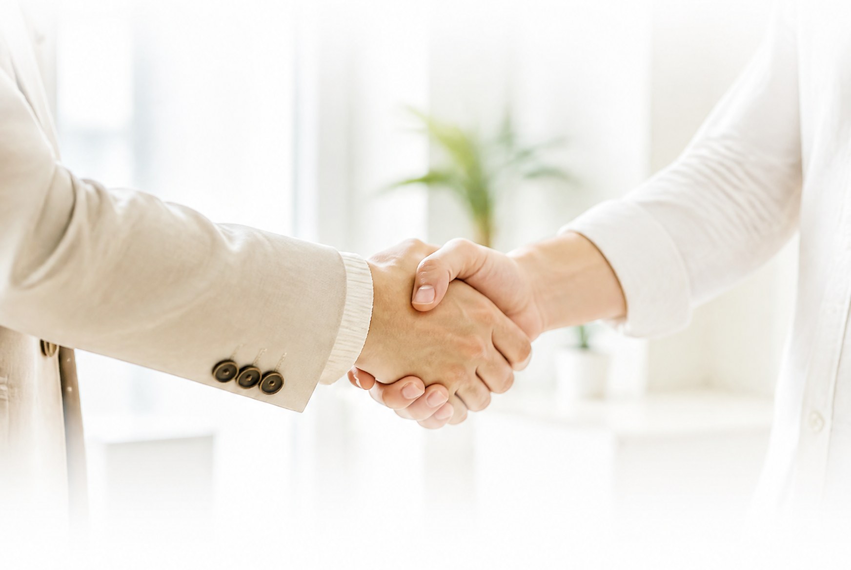Two people shaking hands over a desk in a bright office setting